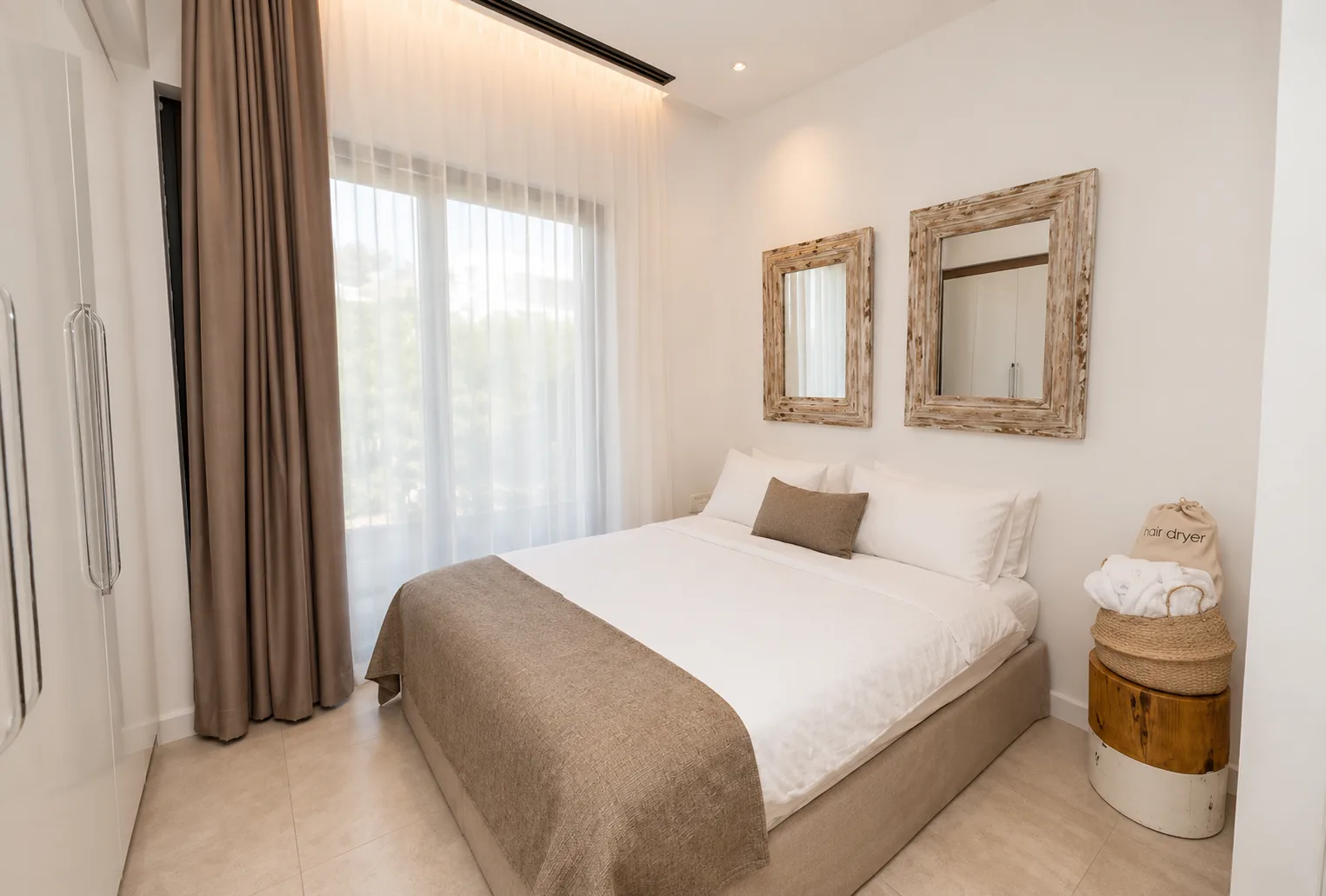Garden View room in quiet linen tones with timber-framed mirrors and soft garden light through the curtains