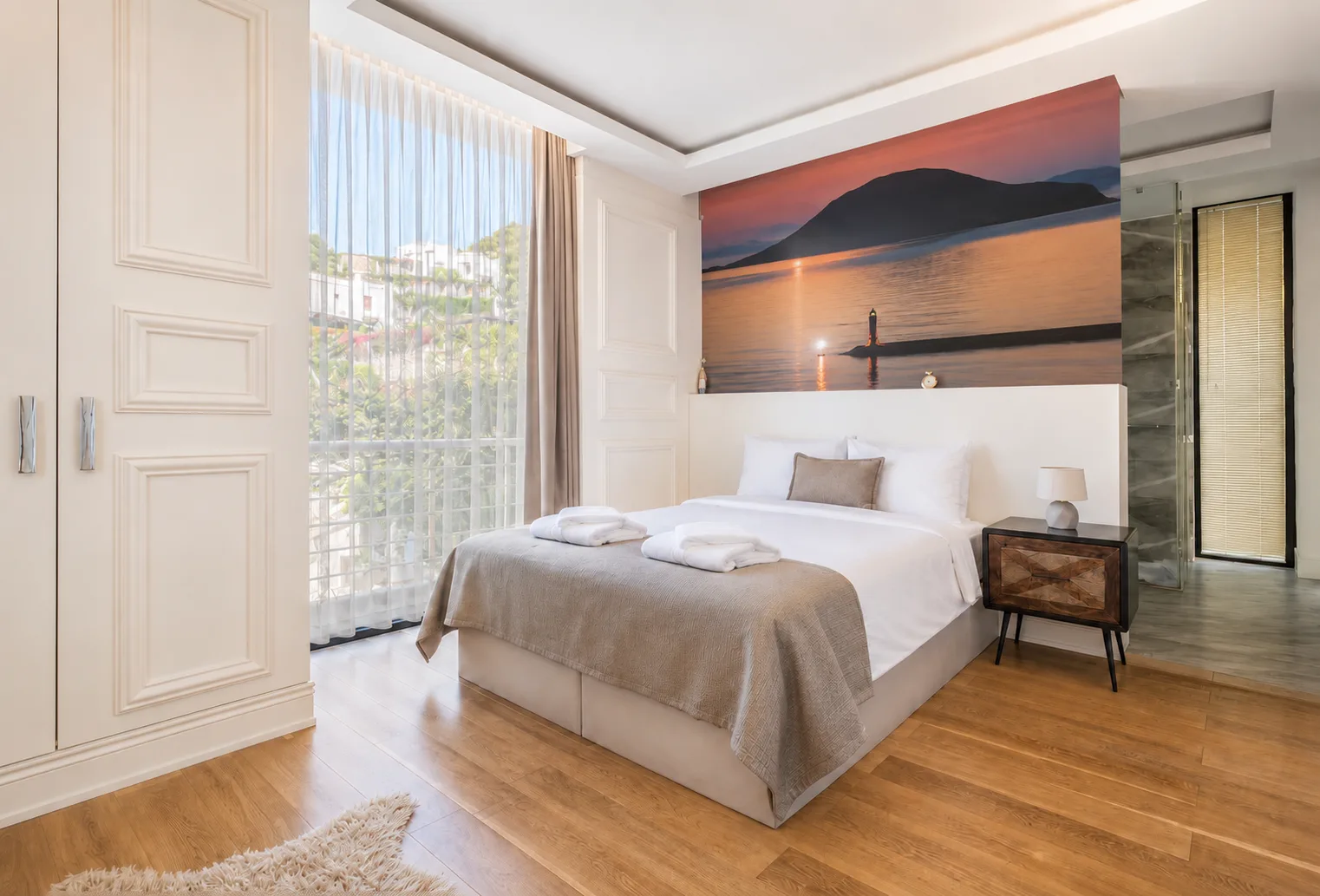 Garden View room with oak floors, panelled cream walls and a sheer-curtained balcony door opening onto the greenery